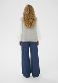Sweat-shirt gris avec manches longues blanches, associé à un pantalon large en denim bleu. Le tissu est doux et la coupe est décontractée.