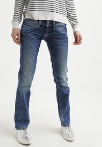 Jeans de mezclilla azul con un acabado descolorido y un diseño de pierna recta, combinados con un suéter a rayas blanco y negro y zapatillas plateadas.