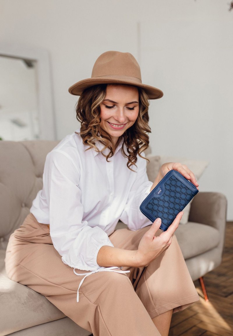 Navyblaue Geldbörse mit strukturiertem Muster, Reißverschluss und kontrastierender Naht, gehalten von einer Person in einem weißen Hemd und beigen Hosen.