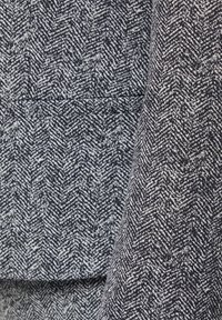 Herringbone patterned fabric in navy and white, displaying a textured finish with a slight sheen and visible weave details.