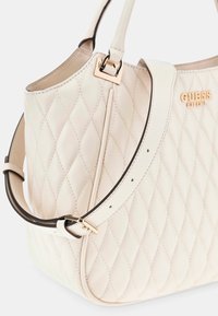 Borsa a tracolla in pelle trapuntata di colore crema con tracolla regolabile, fibbia dorata e logo "GUESS" in oro sul davanti.