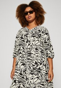 Zebra print dress in black and white; features a V-neckline, three-quarter sleeves, soft fabric, and a loose A-line silhouette.