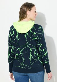 Marineblauwe hoodie met een limoen groen abstract patroon, zacht materiaal, kangoeroezak en een bijpassende limoen groene capuchon.