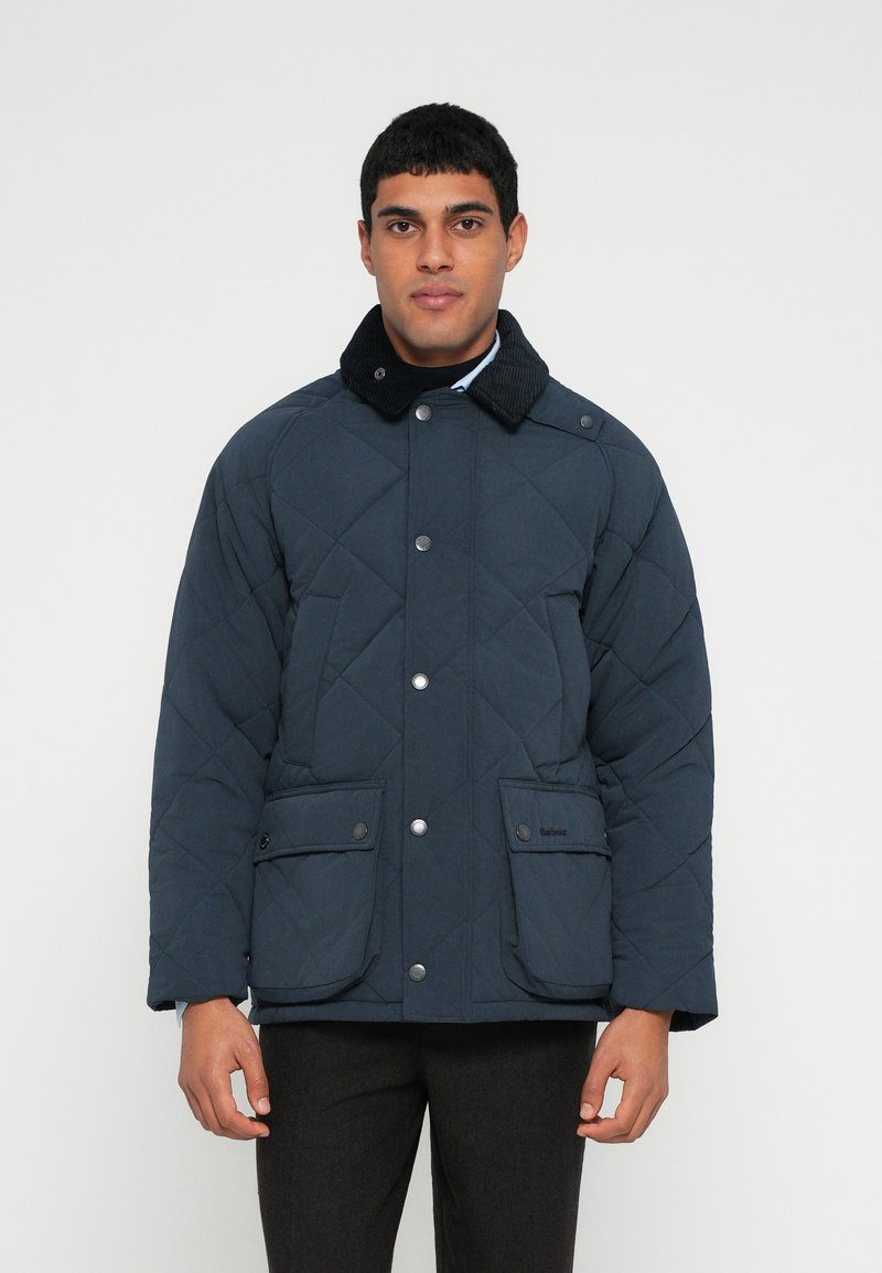 Σκούρο μπλε καπιτονέ μπουφάν με γιακά από κορντό, κουμπιά κούμπωμα με τσιμπιδάκια και δύο εμπρόσθιες τσέπες με καπάκια. Ομαλή υφή, άνετη εφαρμογή.