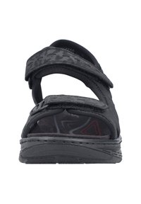 Sandale noire avec des brides Velcro réglables, une semelle intérieure rembourrée et une semelle extérieure en caoutchouc texturé avec un motif géométrique.