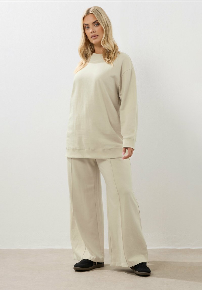 Beige sweatshirt met een relaxed fit, gecombineerd met bijpassende wijde broeken. Gladde stof met minimale stikseldetails, gedragen met donkere instapschoenen.