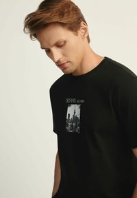 Czarna bawełniana koszulka T-shirt z okrągłym dekoltem i krótkimi rękawami, z graficznym nadrukiem panoramy miasta w odcieniach szarości.