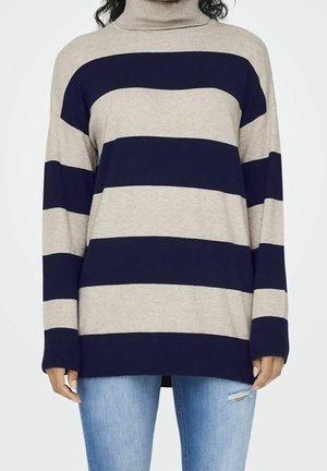Maglione a collo alto a righe con strisce alternate beige e blu navy, con polsini a costine e vestibilità ampia, abbinato a jeans azzurri.