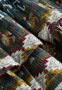 Tissu multicolore présentant des motifs géométriques complexes en rouge, vert et jaune sur un fond bleu foncé, avec des détails texturés et tissés.