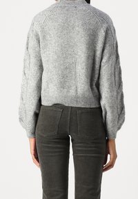 Grijze gebreide trui met een hoge kraag, gestructureerde pofmouwen en een cropped pasvorm, gecombineerd met donkergroene ribfluwelen broek.