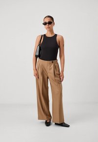 Črn brezrokavnik v obliki bodija, bež široke hlače z visokim pasom in sprednjimi naborki ter črne konične balerinke. Dodatki vključujejo majhno črno torbico in sončna očala.