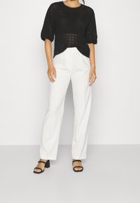 Svart stickad topp med korta ärmar, i kombination med högmidjade vita byxor och svarta klacksandaler med blockklack. Enkel design och textur.