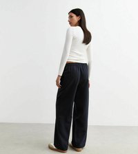 Witte lange mouwen top gecombineerd met brede marineblauwe gestreepte broek. De broek heeft een elastische tailleband en is gestyled met witte sneakers.
