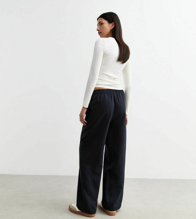 Maglietta bianca a maniche lunghe abbinata a pantaloni ampi a righe blu scuro. I pantaloni presentano una vita elasticizzata e sono abbinati a sneakers bianche.