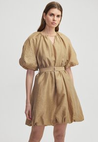 Tan, jurk met pofmouwen, gemaakt van lichtgewicht stof. Kenmerkt zich door een keyhole halslijn, een cinched taille met een riem, en een geraffineerde, uitlopende onderkant.