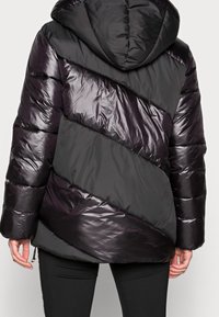 Giacca puffa nera e grigio scuro. Presenta un motivo a zigzag trapuntato, finitura lucida, cappuccio e orlo stretto. Design leggero e caldo.