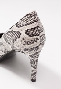 Højhælet sko med sort og hvidt slangeskindsprint, tekstureret materiale, spids tå og slank stiletthæl.