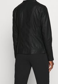 Veste en cuir noir avec un revêtement texturé, des coutures structurées et une coupe ajustée. Le dos est épuré avec une finition nette.