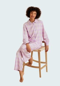 Rosa och lila rutiga pyjamas med knäppkrage, elastiska ärmslut och löst sittande byxor, uppställd på en trästol.