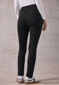 Jeans skinny neri con vita alta, tessuto elasticizzato, dettagli minimali delle tasche posteriori e abbinati a scarpe da ginnastica bianche.