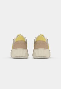 Baskets en suède et en tissu texturé beige et jaune, avec une semelle crême striée et une languette à l'arrière pour un enfilage facile.