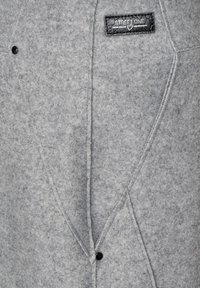 Grå kavaj med en strukturerad design, snedställda stygn, en blank svart knapp och en texturerad svart etikett med "STREET ONE."