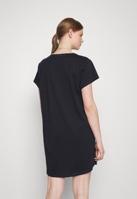 Granatowa sukienka z krótkim rękawem o luźnym kroju i okrągłym dekolcie. Materiał wydaje się miękki, o gładkiej fakturze, z długością sięgającą do połowy uda.