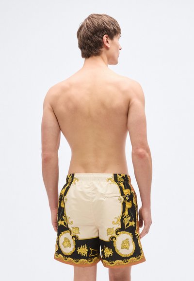 Μαγιό βερμούδα με μαύρο και χρυσό μπαρόκ σχέδιο, που διαθέτει κρεμ πίσω πάνελ, ελαστική μέση και πλαϊνές τσέπες.