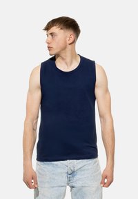 Maglietta senza maniche blu navy in tessuto morbido con scollo rotondo, abbinata a pantaloni corti in denim blu chiaro. Modello di profilo.