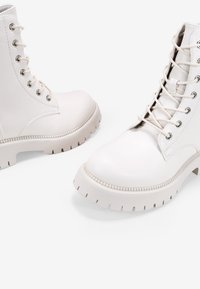 Stivali bianchi con lacci e suola spessa, tomaia in pelle liscia, punta rotonda e occhielli in metallo. Cuciture texturizzate lungo il bordo della suola.