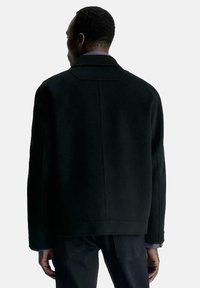 Zwarte jas van wolmix met een rechte snit, grote kraag en minimalistisch design. Voorzien van een enkele achternaad en onopvallende stiksels.