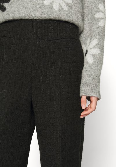 Mørke teksturerede bukser med et diskret ternet mønster og to forlommer, parret med en lysegrå sweater med hvide blomsterdesigns.