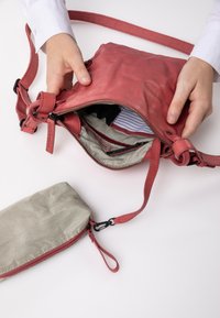 Rote Leder-Crossbody-Tasche mit strukturierter Oberfläche, ausgestattet mit einem Reißverschluss und gefüttertem gestreiften Innenleben. Enthält ein passendes Federmäppchen.