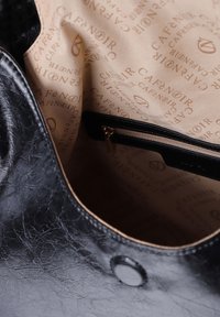 Musta nahkainen käsilaukku, jossa on teksturoitu pinta. Sisäpuolella on beige vuori, jossa on toistuva "Café Noir" -logo ja vetoketjullinen tasku.