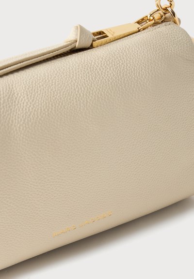 Κρεμ δερμάτινο βραχιόλι με υφή και χρυσαφένιο φερμουάρ και αλυσίδα, με ανάγλυφο λογότυπο "MARC JACOBS" στην κάτω μπροστινή γωνία.