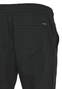 I pantaloni neri presentano un elastico in vita, due tasche posteriori e un piccolo etichetta con la dicitura "Everyday Denim". Sono realizzati in un tessuto leggero con un aspetto testurizzato.