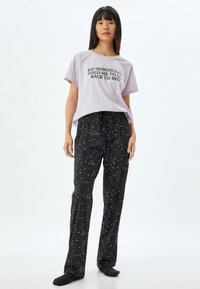 Lichtpaarse T-shirt met korte mouwen en zwarte tekst, gecombineerd met zwarte pyjamabroek met een wit sterren- en sterrenbeeldpatroon.