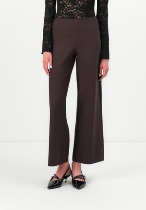 Woman wearing dark brown wide-leg pants, black lace long-sleeve top, and black patent leather pointed-toe heels with straps.