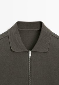 Polo a manica corta verde oliva con cerniera, colletto a coste e tessuto dalla trama liscia. Presenta una chiusura con cerniera argentata.