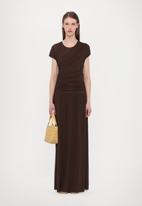 Brun maxi-kjole med korte ermer, med et drapert bodice-design. Kombinert med en flettet gul håndveske. Glatt tekstur, elegant silhuett.