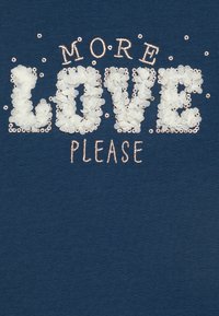 Tejido de color azul marino con la frase "MÁS AMOR POR FAVOR" en letras grandes y esponjosas de color blanco, acentuadas con brillantes lentejuelas y diseños florales.