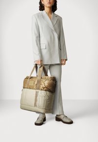 Torba tote w odcieniach beżu i brązu, z podwójnymi uchwytami na górze, zamknięciem na zamek błyskawiczny oraz przednią kieszenią na zamek, o teksturowanej powierzchni.