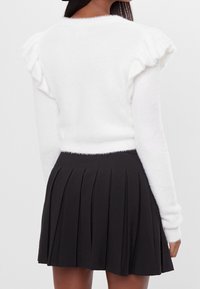 White fluffy sweater with ruffled shoulder accents paired with a black pleated skirt. Sweater has long sleeves and a fitted design.