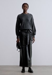 Hall halli kudumissärk, must nahast seelik külje paelaga, must kott ja kingad. Modell seisab neutraalsel taustal.