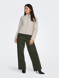 Steppjacke in hellem Beige mit horizontalem Steppmuster, kombiniert mit weitem Olivgrün Cordhosen und schwarzen Stiefeletten mit Absatz.