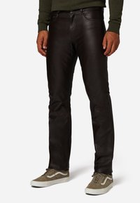 Zwarte leren broek met een slim fit, voorzien van riemlussen en voorzakken, gecombineerd met grijze suède sneakers en een donkere trui.