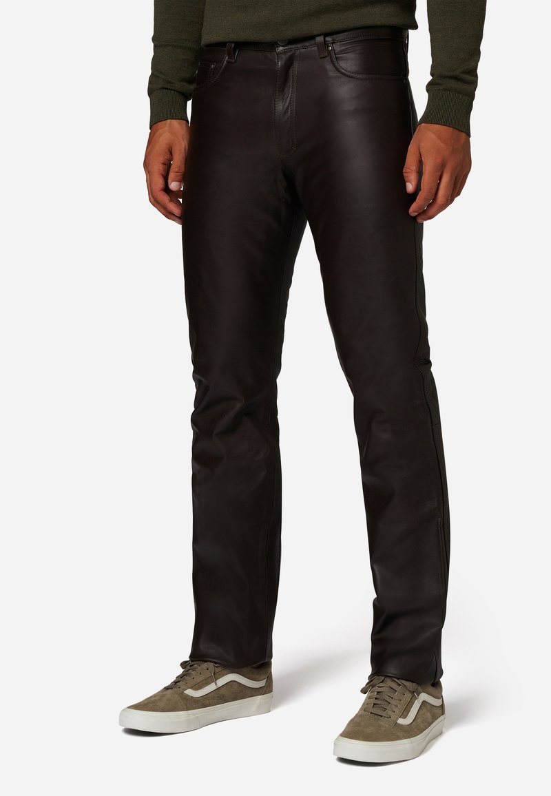 Zwarte leren broek met een slim fit, voorzien van riemlussen en voorzakken, gecombineerd met grijze suède sneakers en een donkere trui.