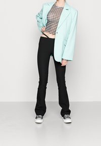 Blazer oversize vert menthe sur un crop top à carreaux noirs, associé à un pantalon noir ajusté évasé et des baskets noir et blanc.