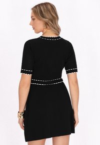 Schwarzes kurzärmeliges Kleid mit weißen Nähten entlang des Ausschnitts und der Taille, das einen taillierten Oberkörper und einen schwingenden Rock hat.