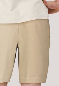 Beige shorts gjorda av ett strukturerat tyg, med rak skärning, sidofickor och en platt midja.